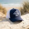 Navy and white Salt Born trucker cap with mesh back and wave logo beach setting